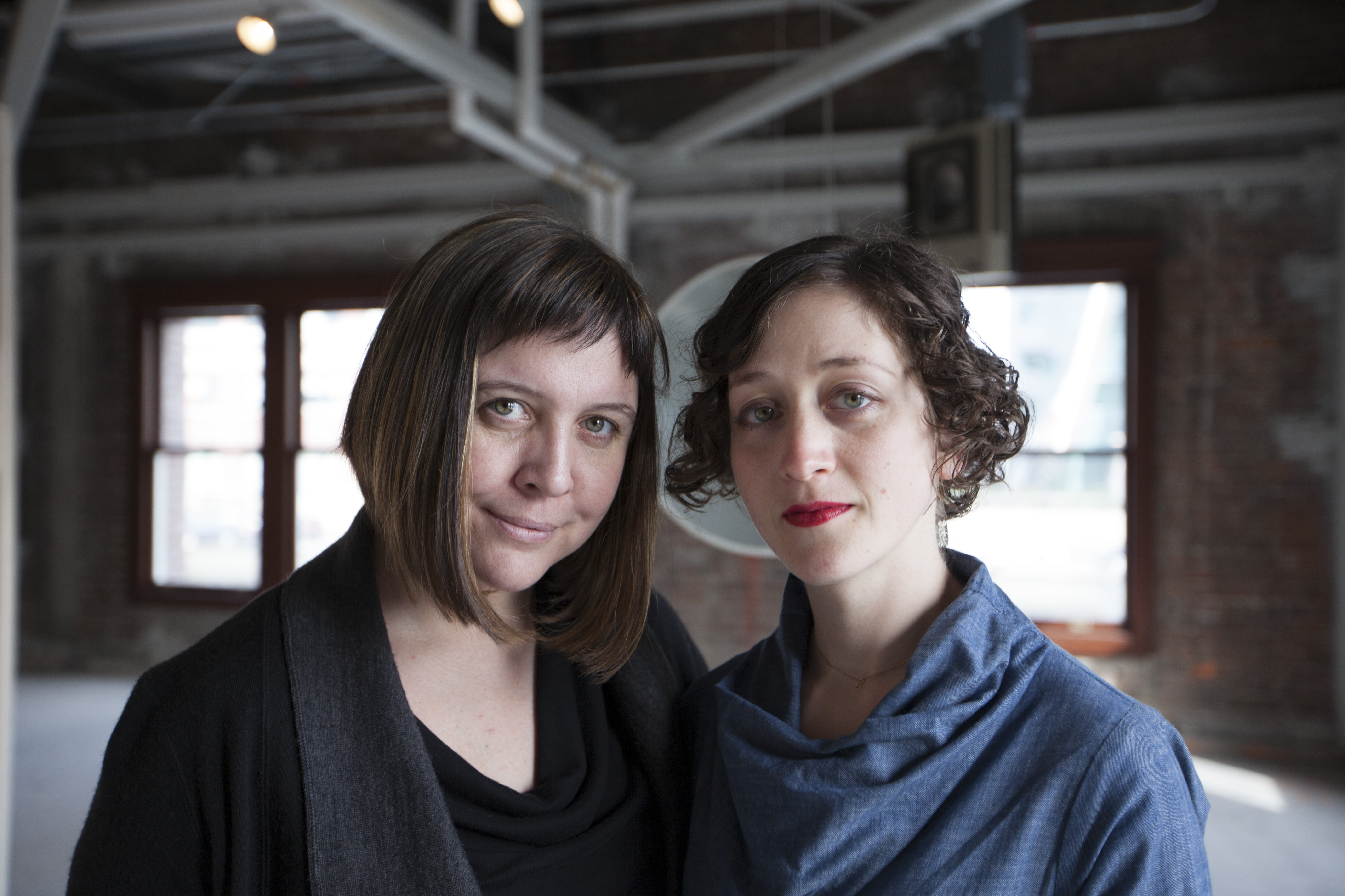 Two women with short brown hair standing in a brightly-lit warehouse space.